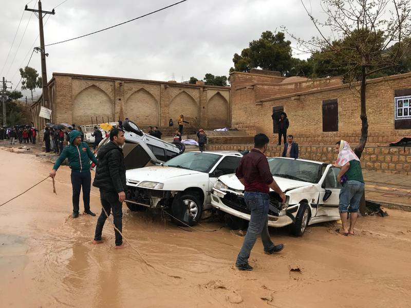People stand near destroyed cars after a flood hit the city of Shiraz. EPA