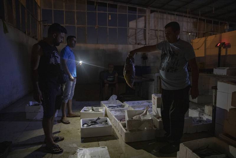 A worker at the city's fish market uses his mobile phone to illuminate the daily catch.