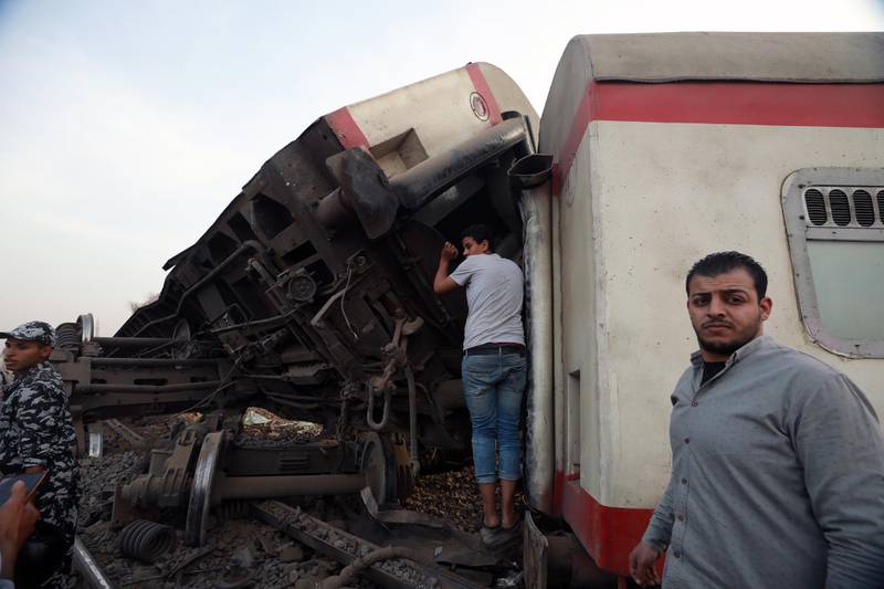 People gather near damaged carriages of a passenger train that was derailed in Toukh, Al Qalyubia Governorate, north of Cairo, Egypt. EPA