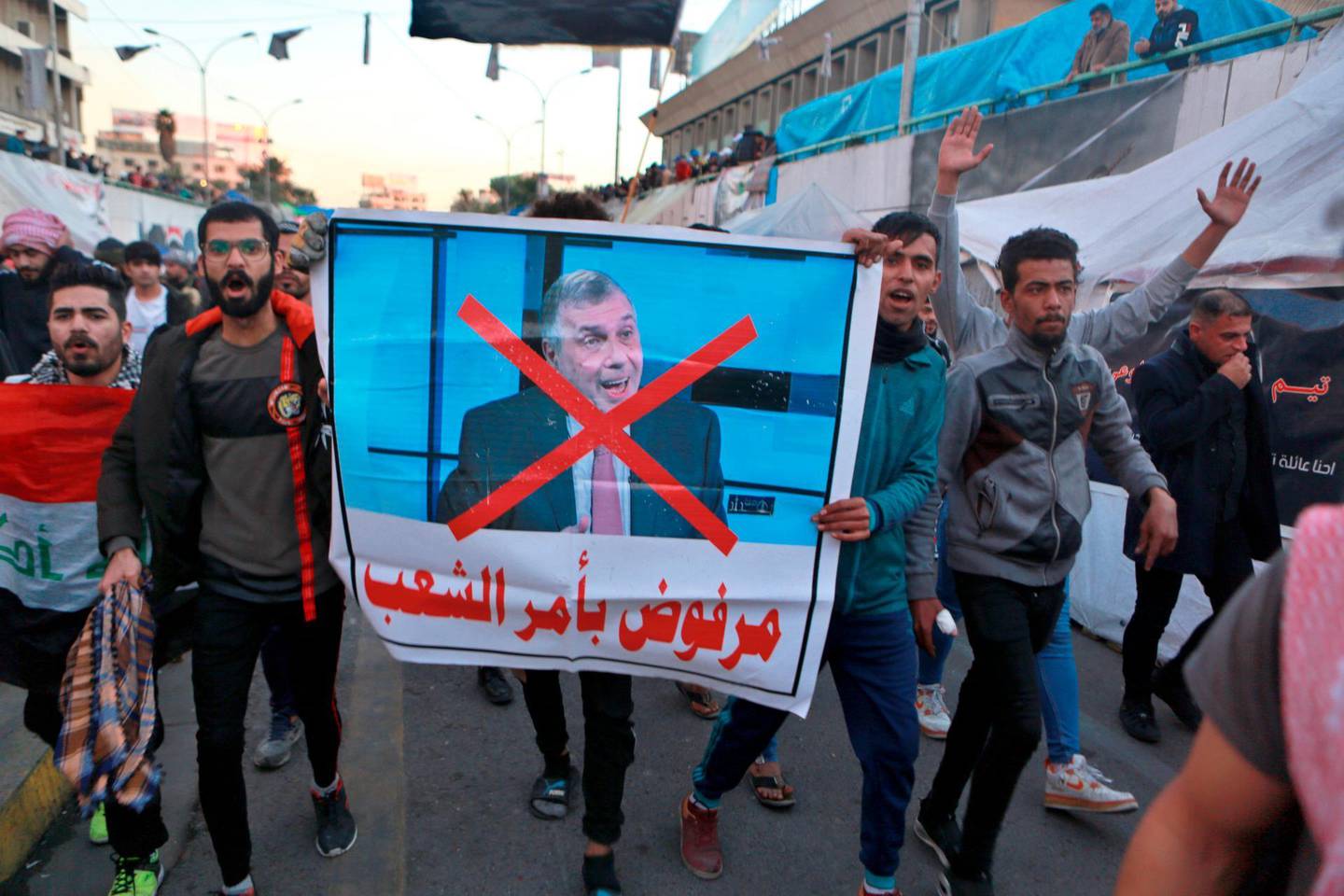 Protesters chant slogans while holding posters of newly appointed Prime Minister Mohammed Allawi with Arabic that reads, "Rejected by the people" during a demonstration in Tahrir Square, Baghdad, Iraq, Sunday, Feb. 2, 2020. Anti-government demonstrators on Sunday rejected Iraq's new prime minister-designate after he was nominated by rival government factions, compounding the challenges he will have to surmount to resolve months of civil unrest. (AP Photo/Khalid Mohammed)