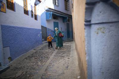 A mother walks with her son down an alleyway deserted of tourists in Chefchaouen, northern Morocco, Saturday, Dec. 26, 2020. The picturesque town, its facades painted in distinctive hues of blue, shut its small population off from the world, and kept the virus out for months. Now, as the country cautiously reopens and tries to resuscitate its struggling economy, Chefchaouen stands subdued, deserted by the tourists that have long been its lifeblood. (AP Photo/Mosa'ab Elshamy)