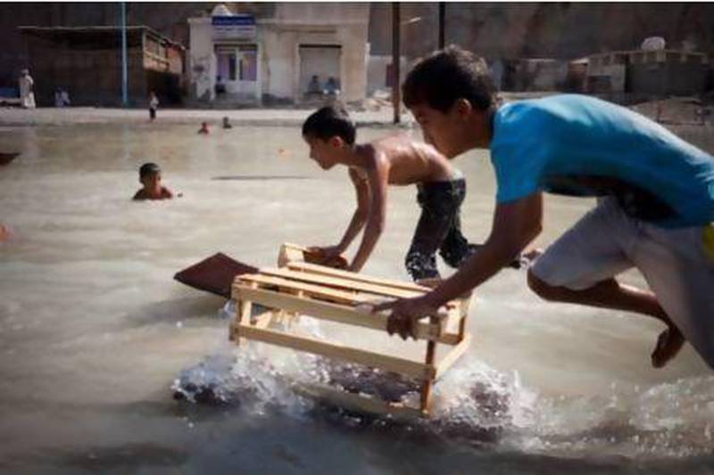 A group of young Kumzari boys cool off by playing and swimming with scrap pieces of wood in a small water hole. Razan Alzayani / The National