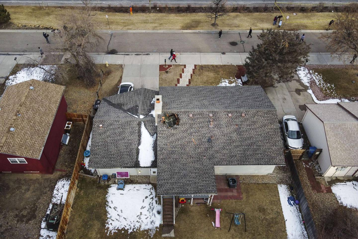BROOMFIELD, CO - FEBRUARY 20: In this aerial view from a drone, people walk past a home with a hole in the roof from falling debris from an airplane engine on February 20, 2021 in Broomfield, Colorado. An engine on the Boeing 777 exploded after takeoff from Denver prompting the flight to return to Denver International Airport where it landed safely.   Michael Ciaglo/Getty Images/AFP
== FOR NEWSPAPERS, INTERNET, TELCOS & TELEVISION USE ONLY ==
