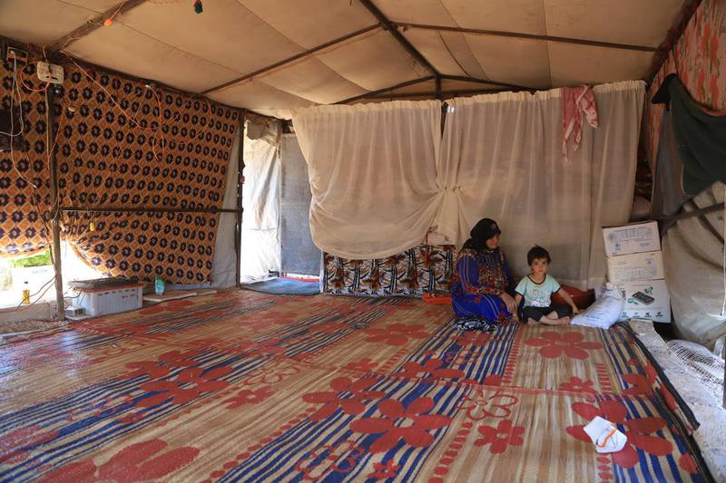 A woman with her grandchild in the free tent of any tools of furniture, patched by blankets to protect them from sun heat.