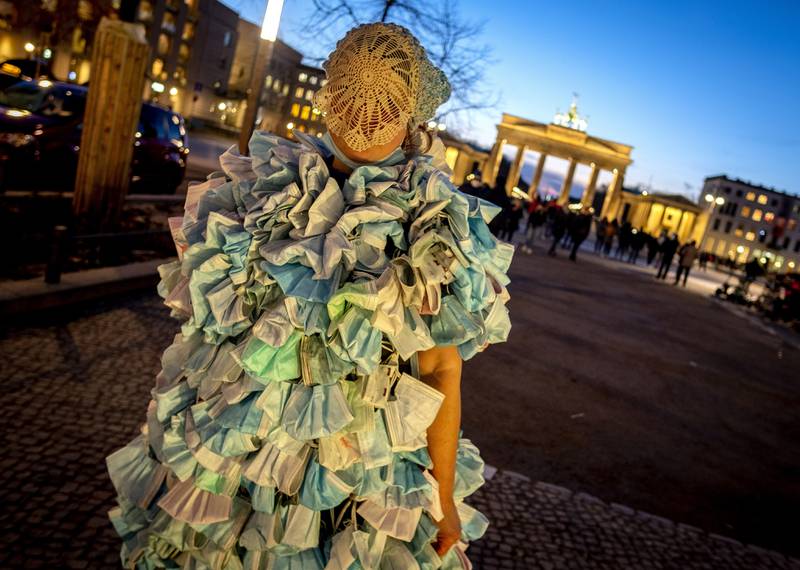 A woman wears a dress made of hundreds of face masks as she returns from an anti- coronavirus demonstration in Berlin.  In the background is the Brandenburg Gate.  AP