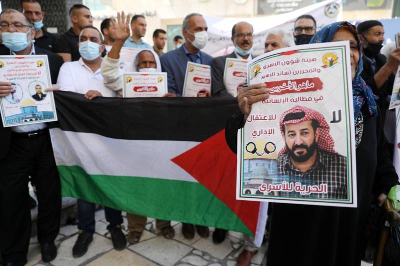 epa08762207 Protesters hold a national flag and posters depicting Palestinian prisoner in Israeli jail Maher al-Akhras during a protest in solidarity with al-Akhras and Palestinian detainees in the West Bank city of Hebron, 21 October 2020. Palestinian protesters and members of the Israeli Neturei Karta movement organized the protest in solidarity with hunger-striking Palestinian detainee Maher al-Akhras and other Palestinians in Israeli prisons. Al-Akhras, 49, is on hunger strike for 87 days in an act of protest against his detention without trial.  EPA/ABED AL HASHLAMOUN