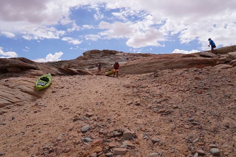 Kayakers carry their boats down the rocky banks of Lake Powell. In normal years, they would be able to float their kayaks off the tarmac ramp.