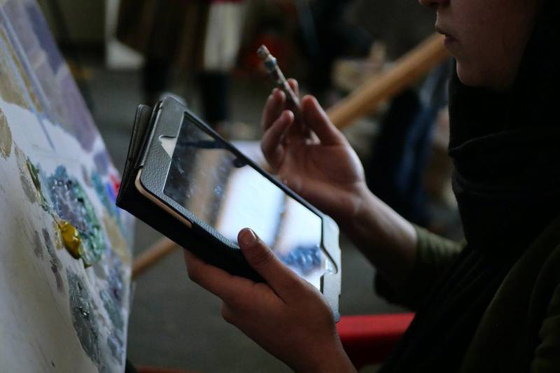 Pictured: A female artist works off a tablet as she paints onto a canvas at the ArtLords headquarters in Kabul. Photo by Charlie Faulkner February 2021