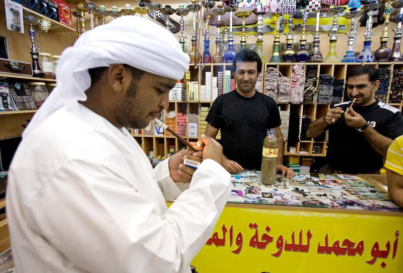 Abu Dhabi - November 23, 2008:  A customer lights up Dokha (tobacco) in his Medwakh (pipe aka Medvakh) while Fahyad Haftrangi watches and Ebrahim Torabpouran lights his own Medwakh in the 43-year-od Abu Muhammad's Smoke Shop in Abu Dhabi, November 23, 2008. (Jeff Topping/The National) *** Local Caption ***  JT003-1125-SMOKE SHOP IMG_1349.jpgJT003-1125-SMOKE SHOP IMG_1349.jpg