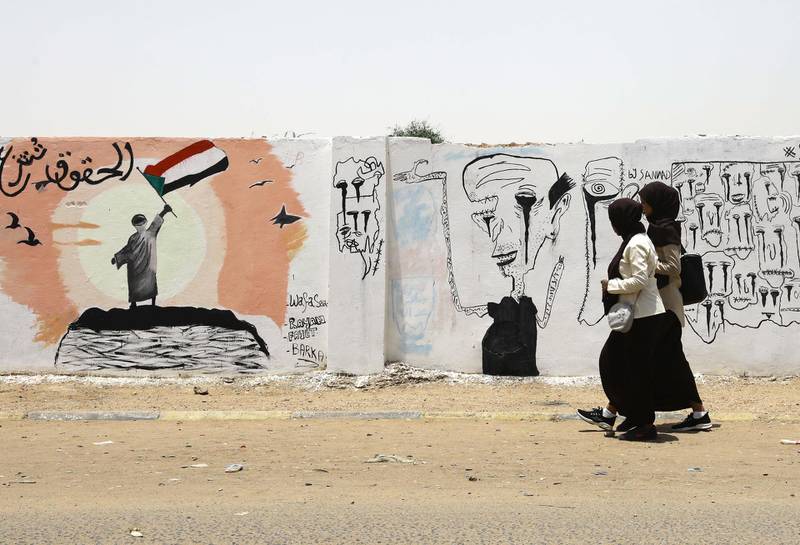 Sudanese girls walk by walls depicting the uprising. EPA
