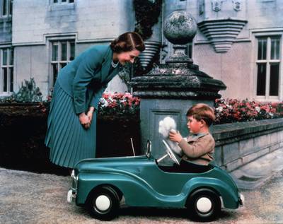 Queen Elizabeth watches her son Prince Charles driving a toy car in the grounds of Balmoral Castle in 1952 