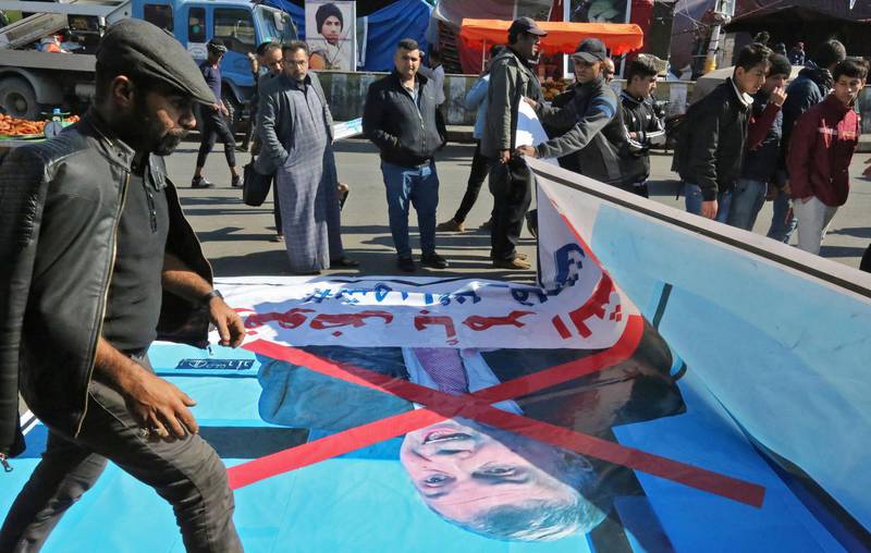 An Iraqi anti-government demonstrators looks at a poster bearing the portrait of prime minister-designate Mohammad Allawi with a red X over it in Baghdad's Tahrir square on February 3, 2020. Furious anti-government youth in Iraq's capital and south rejected the nomination of Mohammad Allawi as prime minister, but came up against rival sit-ins by supporters of an influential cleric backing the new premier. / AFP / SABAH ARAR
