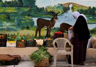 A woman buys vegetables near one of Bibani's murals