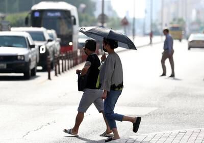 People take cover from the sun with an umbrella on a hot day in Dubai. Chris Whiteoak / The National