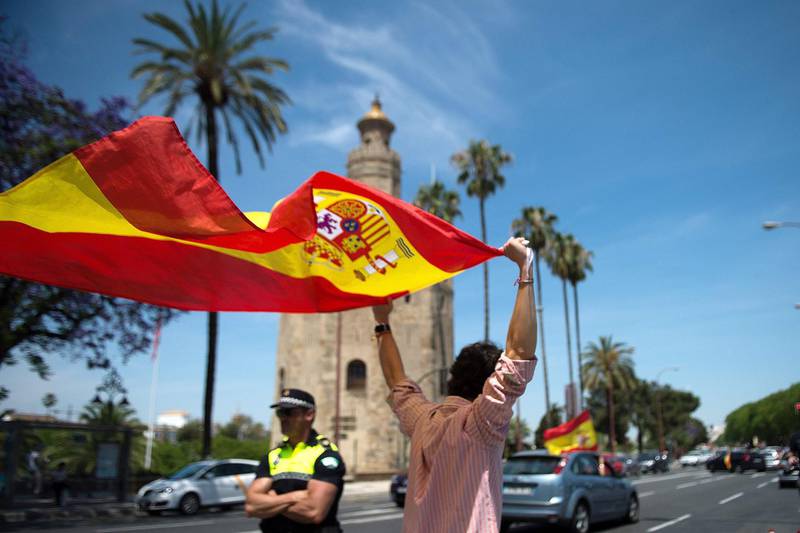 A demonstrator wearing a face mask waves a Spanish flag during a "caravan for Spain and its freedom" protest by far-right party Vox in Sevilla on May 23, 2020. Spain, one of the most affected countries in the world by the novel coronavirus with 28,628 fatalities, has extended until June 6 the state of emergency which significantly limits the freedom of movement to fight the epidemic. The left-wing government's management of the crisis has drawn a barrage of criticism from righ-wing parties who have denounced its "brutal confinement". / AFP / CRISTINA QUICLER
