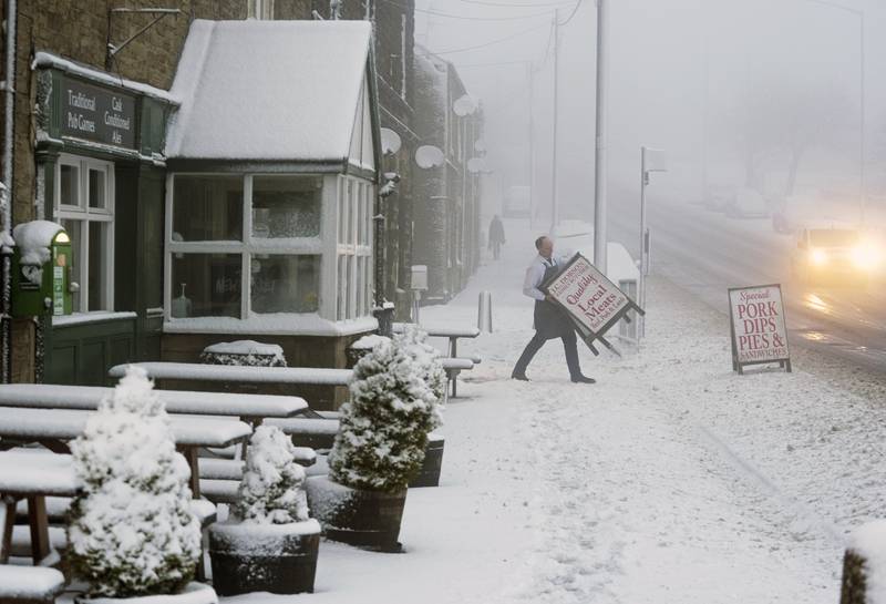 A local butcher carries his shop sign across a snowy pavement in Tow Law, County Durham, north-east England, after wintry weather had hit much of the country. PA