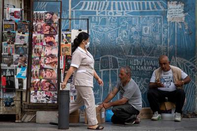 A maid from the Philippines wears a mask to help stop the spread of the new coronavirus as she walks in front of a newspaper kiosk in central Beirut's commercial Hamra Street, in Beirut, Lebanon, Wednesday, May 20, 2020. (AP Photo/Hassan Ammar)