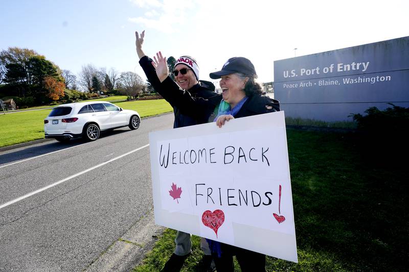 Dual US-Canadian citizen Traysi Spring and her American husband, Tom Bakken, hold a homemade sign to welcome people heading into the US from Canada. AP