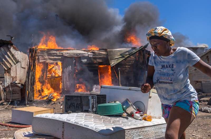 A resident tried to salvage some belongings as a fire rages through shacks in Masiphumelele, Cape Town, South Africa. The cause of the blaze remains unknown. EPA