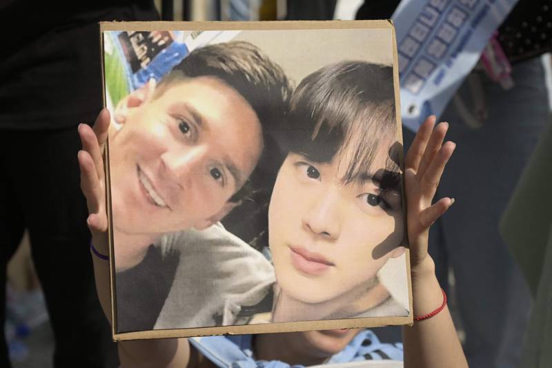 A BTS fans holds an image of Argentine footballer Lionel Messi, left, with BTS member Jin. 