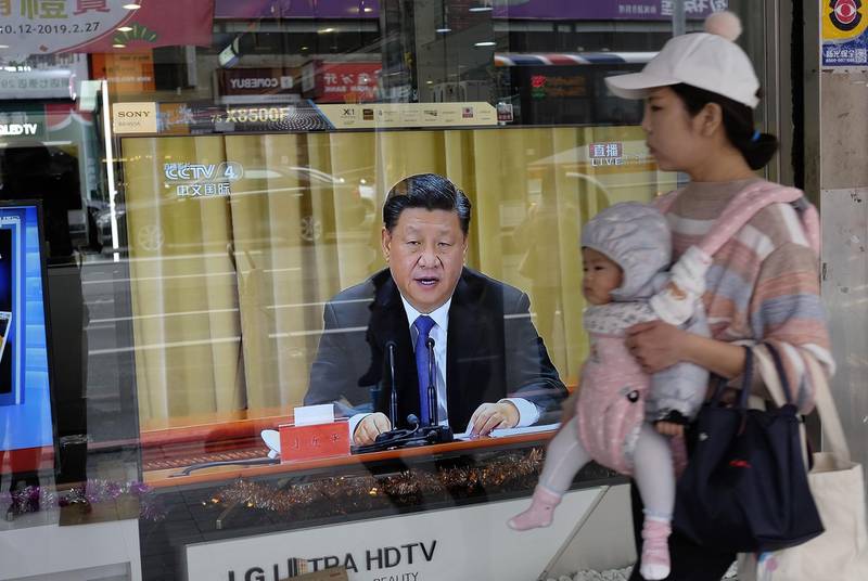 A mother carries her child past a television in New Taipei City on January 2, 2019 showing China's leader Xi Jinping making a speech commemorating the 40th anniversary of a message sent to Taiwan in 1979. Taiwan's unification with the mainland is "inevitable", President Xi Jinping said on January 2, warning against any efforts to promote the island's independence and saying China would not renounce the option of using military force to bring it into the fold. / AFP / Sam YEH
