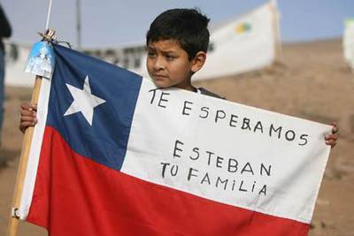 A young boy holds a Chilean flag reading "We wait for you Esteban, Your Family" during celebrations after one of the drills working to rescue the 33 finally reached their shelter in the San Jose mine play at La Esperanza encampment, near Copiapo, Chile, October 9, 2010. After a record two months trapped underground in a collapsed mine, the miners appear to be just days from a miraculous rescue AFP PHOTO/HECTOR RETAMAL