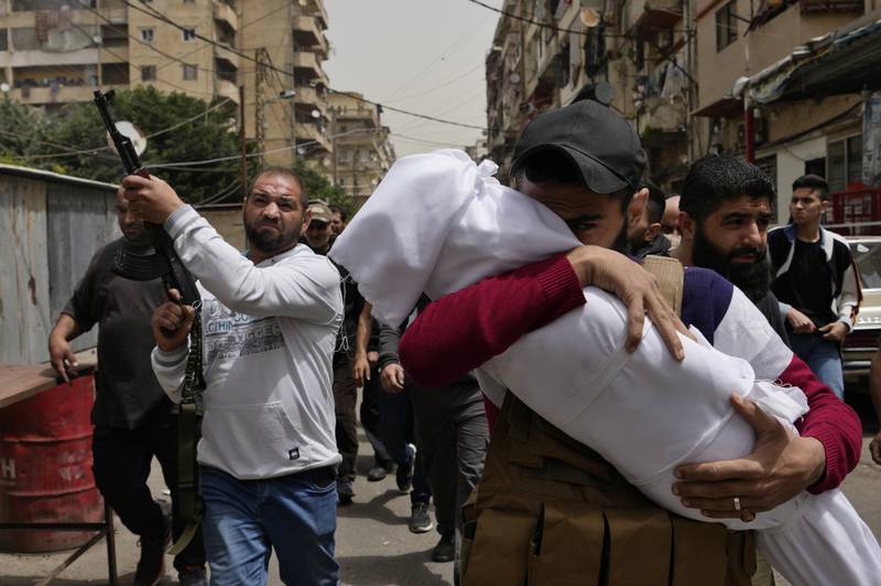 A man carries the body of a young girl who died when the boat sank, as a mourner fires in the air during the funeral procession. AP Photo
