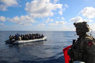 In this image provided by the Turkish Military, a member of Turkish forces, right, on a boat approaches migrants aboard a dinghy in the mid Mediterranean Sea, Wednesday, Jan. 29, 2020. The military said that a military ship, TCG Gaziantep, assisted the migrants and provided medical aid before handing them over to the Libyan Coast Guard. The frigate is in the region to support NATO's Mediterranean Shield Operation and to assist NATO's Marine Guard Operation. (Turkish Military via AP)