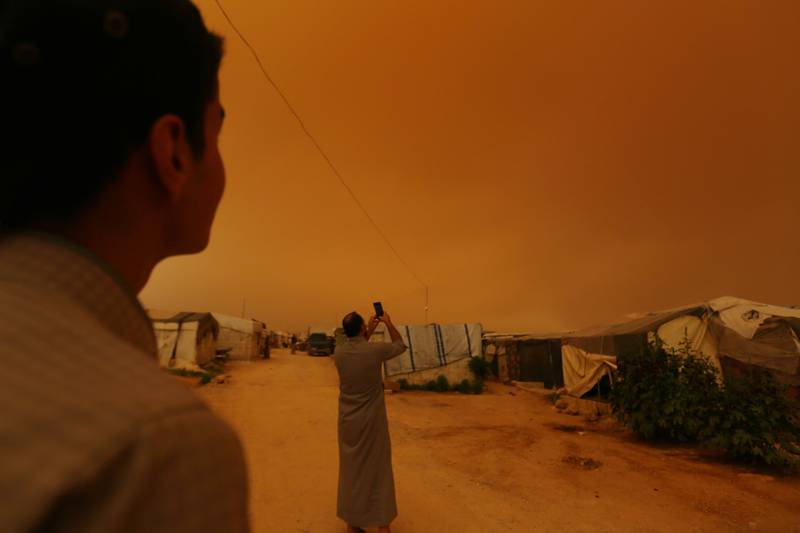 A displaced Syrian takes a picture of the sky during a dust storm in Dana. AFP