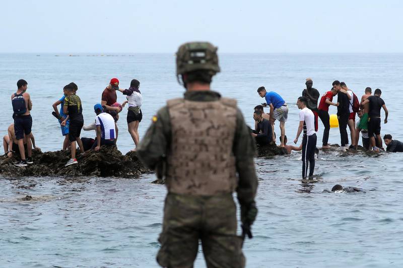 A Spanish soldier stands in front of Moroccan migrants. Reuters