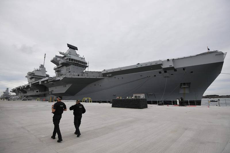 (FILES) In this file photo taken on August 16, 2017 Armed police officers patrol the quayside next to the moored  65,000-tonne British aircraft carrier HMS Queen Elizabeth after it arrived at Portsmouth Naval base, its new home port, Portsmouth, southern England. Prime Minister Boris Johnson will on Thursday, November 19, unveil what is being billed as Britain's biggest programme of investment in the armed forces since the end of the Cold War. / AFP / Ben STANSALL
