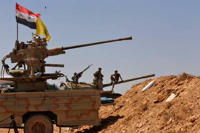 Syrian forces members stand on a tank next to vehicles waiting to transport Islamic State (IS) group members in the Qara area in Syria's Qalamoun region on August 28, 2017 as part of a deal between Hezbollah and IS fighters where the jihadists would leave to eastern Syria.Syria's state news agency SANA, quoting a military source, confirmed Hezbollah and IS had agreed that "the remaining Daesh (IS) fighters will leave to eastern Syria". And a Lebanese military source told AFP the jihadist group would quit territory it held in eastern Lebanon. / AFP PHOTO / Louai Beshara