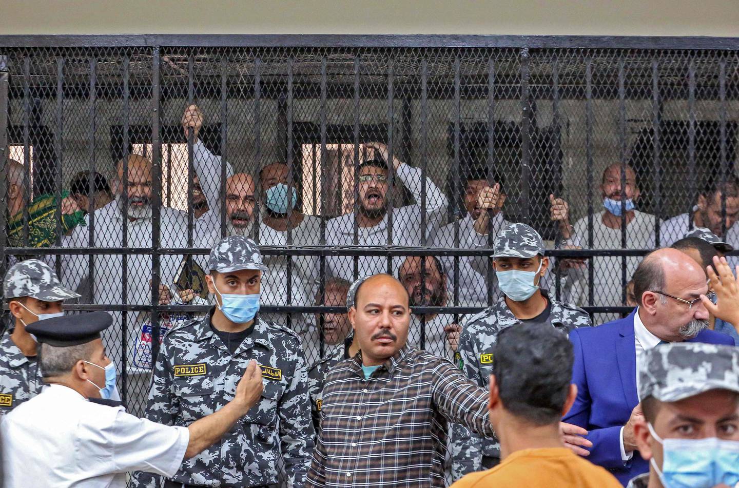 Men charged with illegal excavation and trafficking of antiquities react in the accused dock during the verdict announcement session of their trial in Egypt's capital Cairo on April 21, 2022.  - The court handed Egyptian businessman Hassan Ratib a five-year jail sentence, and former MP Alaa Hassanein (standing-L) 10 years, local media reported.  (Photo by Khaled KAMEL  /  AFP)