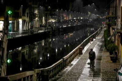 A man stands on the unusually empty Navigli area, a popular spot of restaurants and pubs alongside canals in Milan, Italy,  as authorities imposed curfews. AP