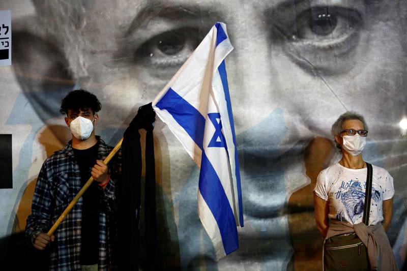 A man wearing a protective face mask holds an Israel's flag as Israelis demonstrate against Israel's Prime Minister Benjamin Netanyahu, under strict restrictions made to slow down the Covid-19 spread, on Rabin Square in Tel Aviv, Israel April 19, 2020 REUTERS