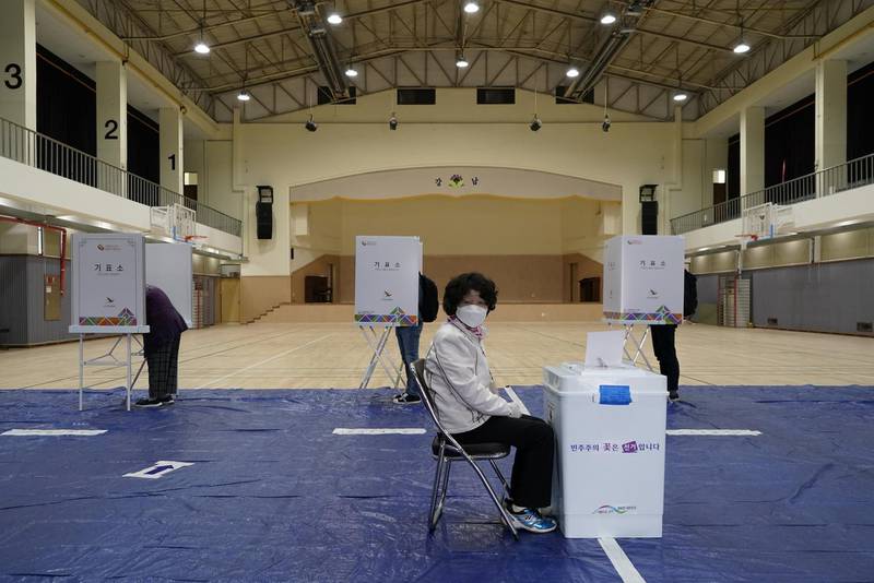 An electoral worker wearing a face mask waits as voters fill in ballots at polling booths in Seoul, South Korea. Reuters