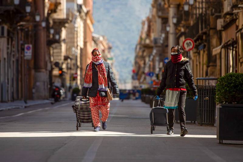Pedestrians pull trolley bags along a nearly deserted street in Palermo, Italy.  Bloomberg