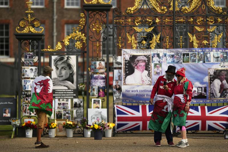 People wearing the Welsh flag stand in front of portraits and messages of remembrance for Princess Diana displayed on the gates of Kensington Palace. AP