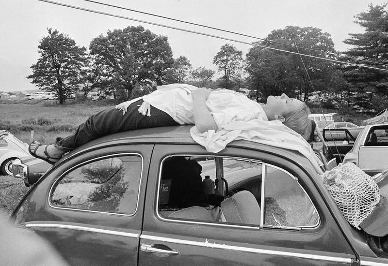 A young woman naps on top of her car. AP Photo