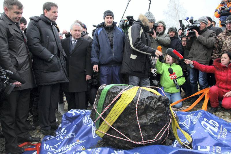 People look at what scientists believe to be a chunk of the Chelyabinsk meteor, recovered from Chebarkul Lake near Chelyabinsk, about 1500 kilometers (930 miles) east of Moscow,  Russia, Wednesday, Oct. 16, 2013. Scientists on Wednesday recovered what could be the largest part of this meteor from Chebarkul Lake outside the city. They weighed it using a giant steelyard balance, which displayed 570 kilograms (1,256 pounds) before it broke. (AP Photo/Alexander Firsov)