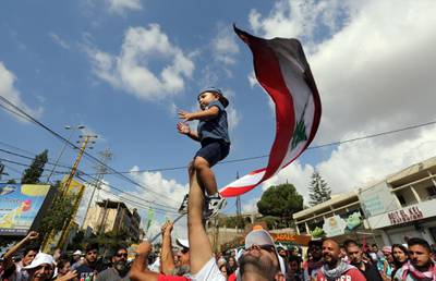 A man lifts a child as demonstrators chant and carry national flags during an anti-government protest in the southern city of Nabatiyeh.
