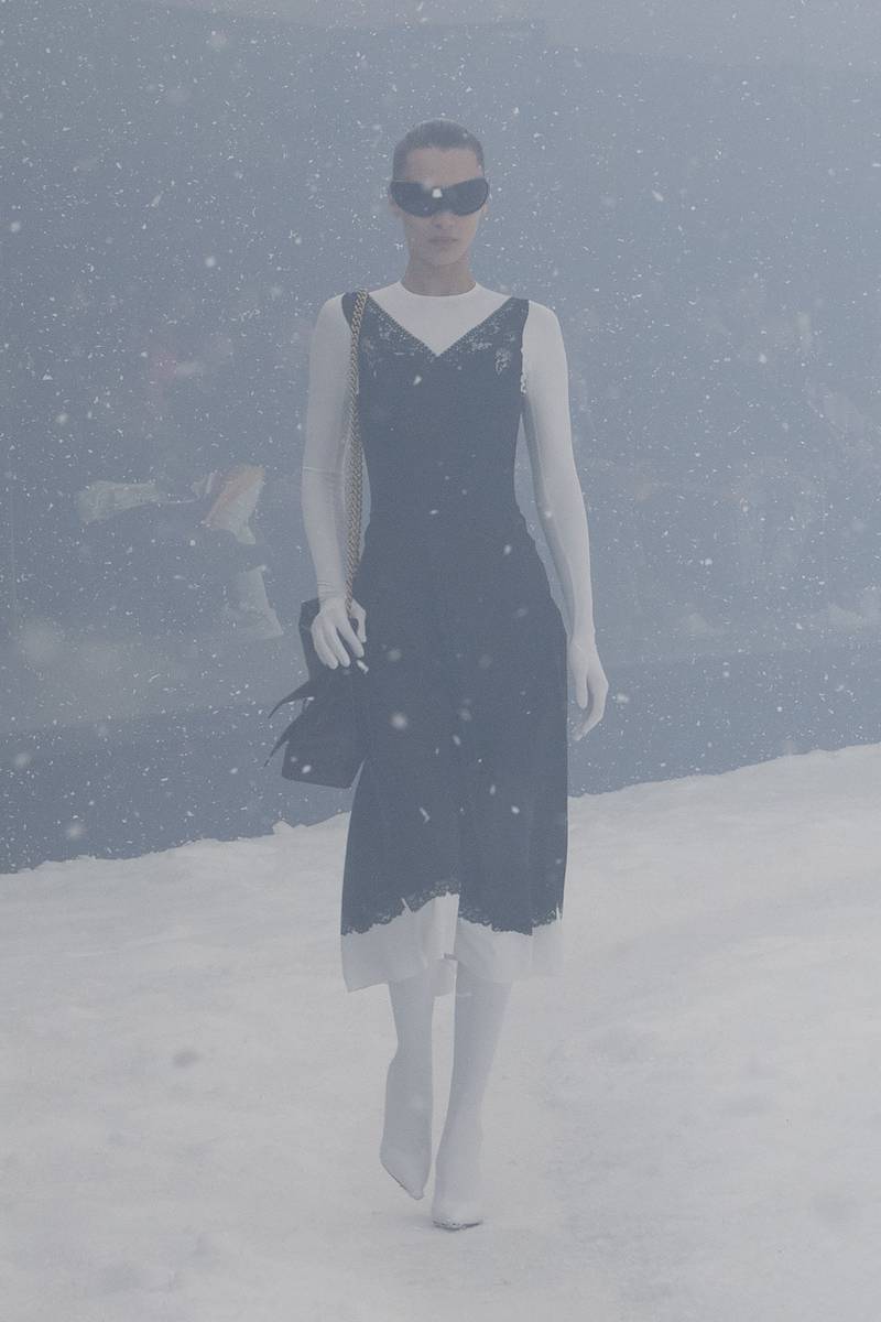 A model wears a white body suit under a black dress.