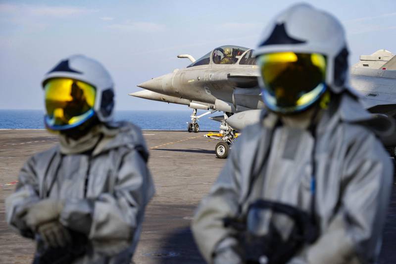 Fighter jets on the flight deck, as navy personnel stand by  