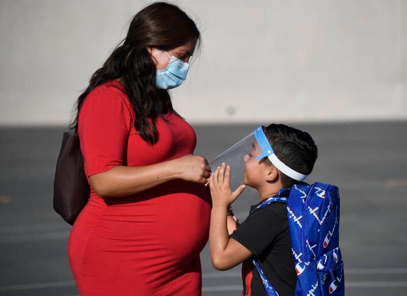 A parent adjusts her son's visor on the first day of school at Enrique Camarena Elementary School in Chula Vista, California, on July 21, 2021. AP