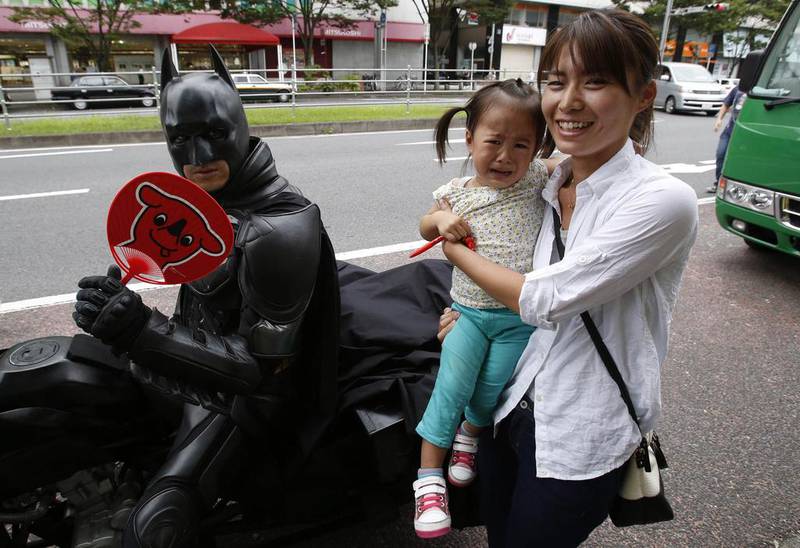 A woman carrying a crying child poses for pictures next to a 41-year-old man going by the name of Chibatman sitting on his Chibatpod. 
