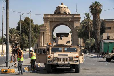 Municipality workers clean up while Iraqi army soldiers guard the entrance to the Green Zone. AFP