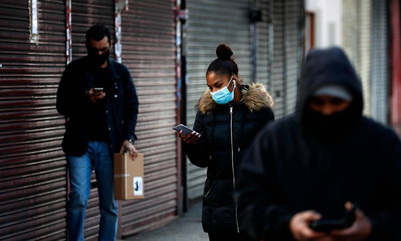 People look at their mobile phones as they walk past closed shops in London. AP Photo