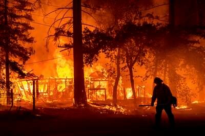 A firefighter passes a burning home as the Dixie Fire flares in Plumas County, California.
