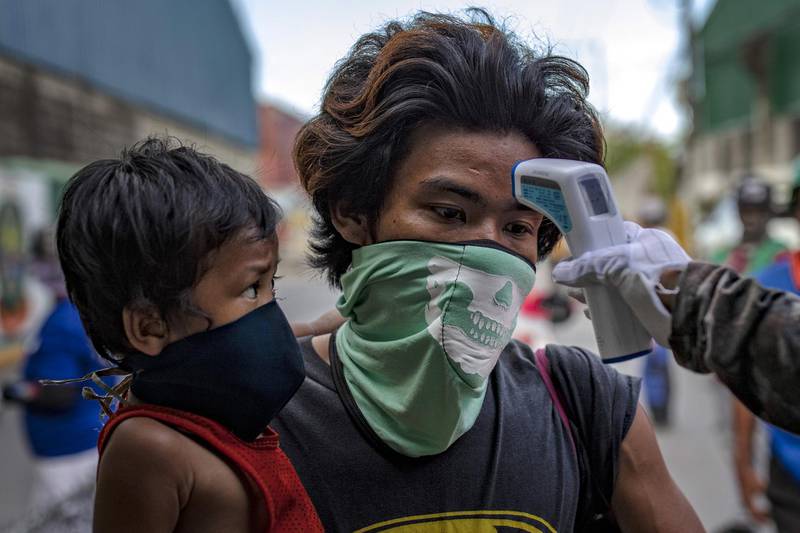 A man and his son wear has their temperature checked before being allowed to enter a slum area in Manila, Philippines. Getty Images