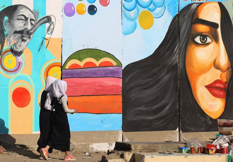 Iraqi women walk in front of a mural inspired by ongoing anti-government protests, in Tahrir square in the capital Baghdad, on December 19, 2019. Iraqi political leaders face a midnight deadline today to choose a new prime minister to run a country shaken by months of unprecedented street protests that have left hundreds dead. / AFP / AHMAD AL-RUBAYE
